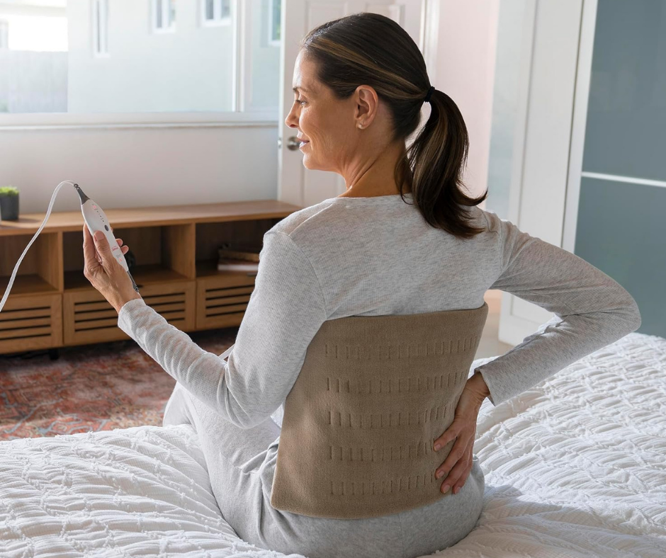 Woman wearing a king size heating pad on her back while holding the heat control