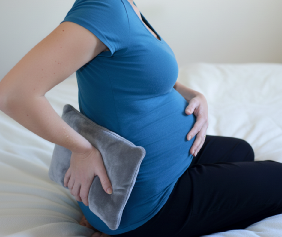 Pregnant woman using a low-heat heating pad on the lower back for localized muscle relief, face not shown